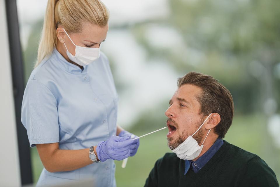 A nurse in gloves and a mask taking a sample from a seated patient