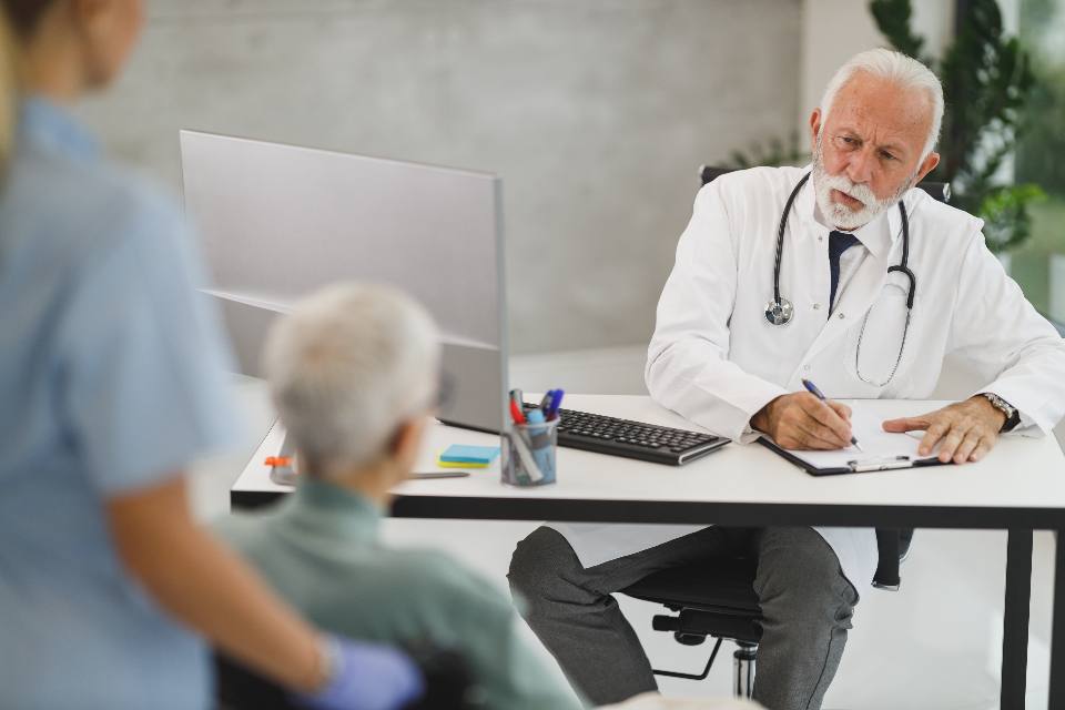 A doctor writing notes at his desk while a patient sits across from him
